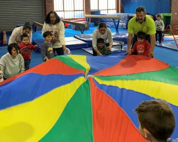 Children and adults play with gymnastics parachute