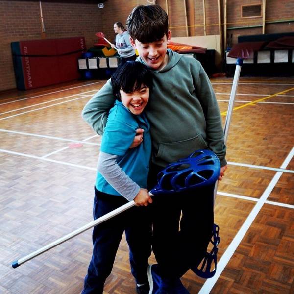 Two kids hugging and smiling and holding lacrosse sticks